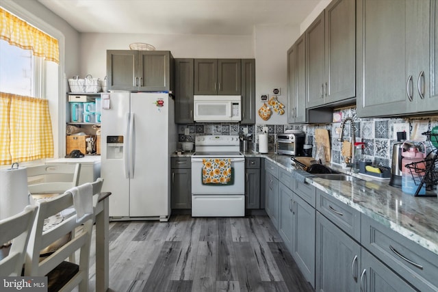 kitchen with sink, gray cabinets, white appliances, hardwood / wood-style floors, and backsplash