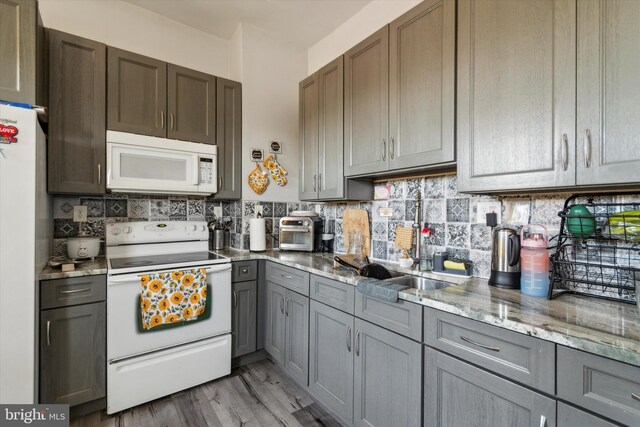 kitchen with white appliances, light hardwood / wood-style flooring, decorative backsplash, and light stone countertops