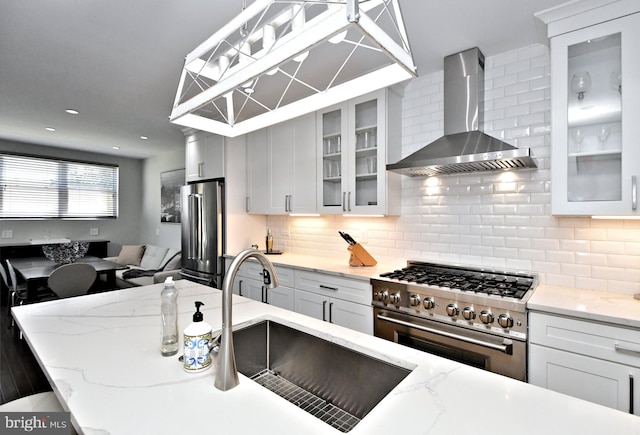 kitchen with light stone counters, wall chimney exhaust hood, white cabinets, and high quality appliances