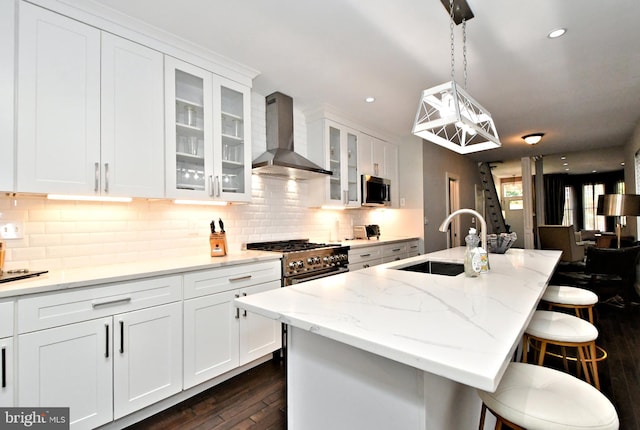 kitchen featuring decorative light fixtures, wall chimney exhaust hood, a kitchen island with sink, a breakfast bar, and stainless steel appliances