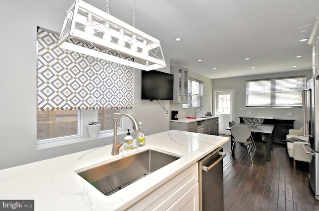 kitchen with dark hardwood / wood-style flooring, appliances with stainless steel finishes, hanging light fixtures, sink, and light stone counters