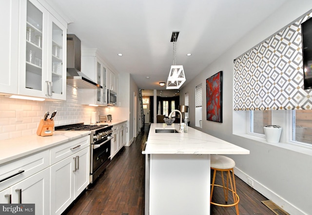 kitchen with stainless steel appliances, decorative light fixtures, sink, wall chimney exhaust hood, and a breakfast bar area