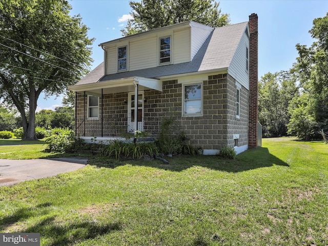 view of front facade with covered porch, a chimney, and a front lawn