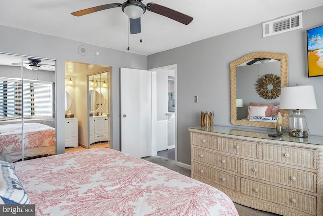 bedroom with dark colored carpet, visible vents, ensuite bathroom, a ceiling fan, and baseboards