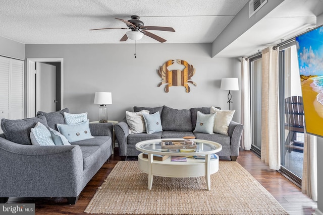 living room with ceiling fan, visible vents, dark wood finished floors, and a textured ceiling