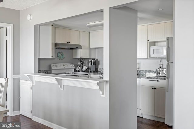 kitchen with white appliances, under cabinet range hood, white cabinetry, and dark wood finished floors