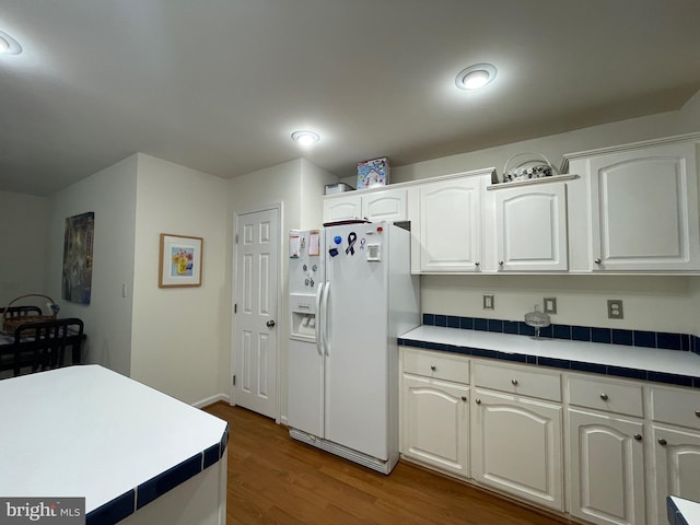 kitchen featuring dark wood-type flooring, tile counters, white fridge with ice dispenser, and white cabinetry