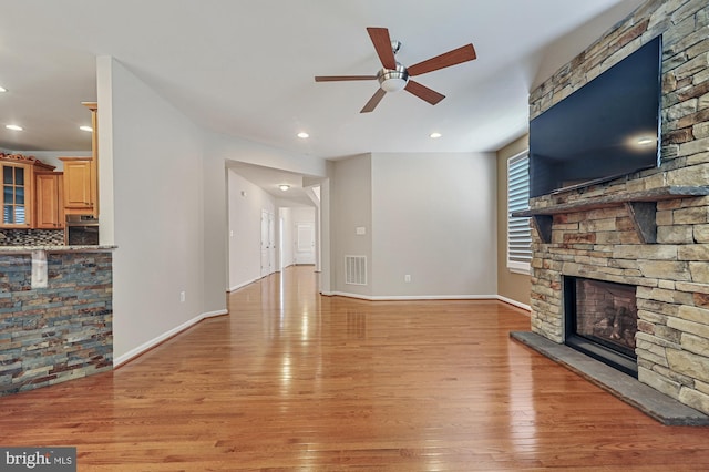 living room with ceiling fan, light hardwood / wood-style flooring, and a stone fireplace