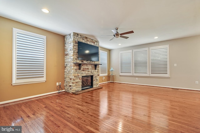 unfurnished living room featuring ceiling fan, brick wall, a stone fireplace, and hardwood / wood-style flooring