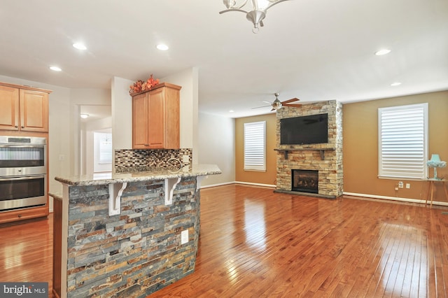 kitchen with a fireplace, double oven, hardwood / wood-style flooring, ceiling fan, and decorative backsplash