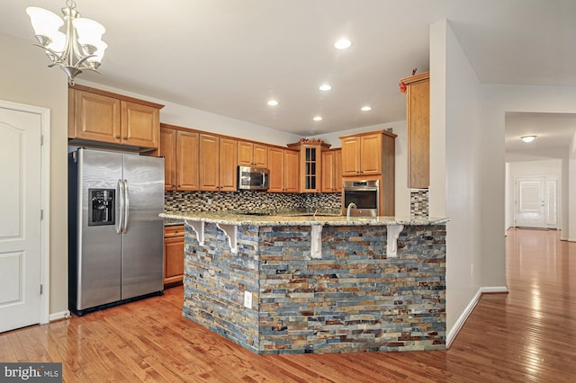 kitchen featuring decorative backsplash, appliances with stainless steel finishes, light stone countertops, light wood-type flooring, and kitchen peninsula