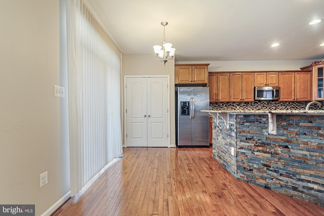 kitchen featuring appliances with stainless steel finishes, backsplash, sink, an inviting chandelier, and light hardwood / wood-style flooring