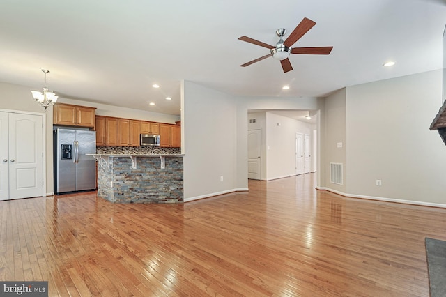 unfurnished living room featuring ceiling fan with notable chandelier and light wood-type flooring