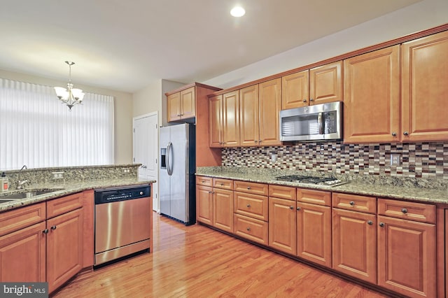 kitchen featuring light wood-type flooring, pendant lighting, a notable chandelier, appliances with stainless steel finishes, and light stone counters