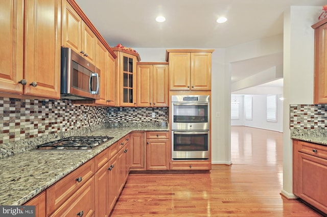 kitchen with decorative backsplash, stainless steel appliances, light stone counters, and light hardwood / wood-style floors