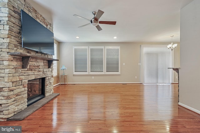 unfurnished living room featuring ceiling fan with notable chandelier, a stone fireplace, and hardwood / wood-style floors