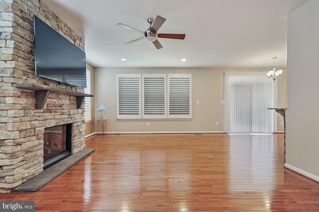 unfurnished living room featuring a stone fireplace, ceiling fan with notable chandelier, and light wood-type flooring