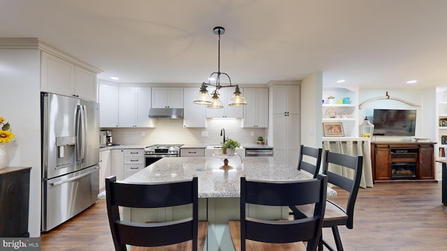 kitchen with appliances with stainless steel finishes, hardwood / wood-style flooring, a center island, and light stone countertops