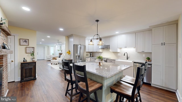 kitchen featuring stainless steel appliances, a brick fireplace, decorative backsplash, dark wood-type flooring, and decorative light fixtures