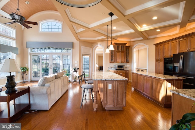 kitchen featuring black appliances, a kitchen island, brown cabinetry, and open floor plan