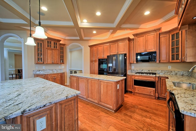 kitchen with arched walkways, a kitchen island, hanging light fixtures, black appliances, and glass insert cabinets