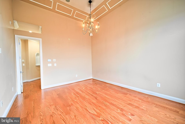 unfurnished room with a chandelier, wood finished floors, and baseboards