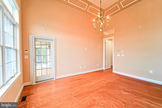 spare room featuring an inviting chandelier, baseboards, a high ceiling, and visible vents