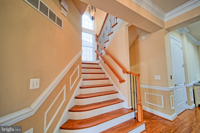 stairs featuring wood finished floors, visible vents, and crown molding