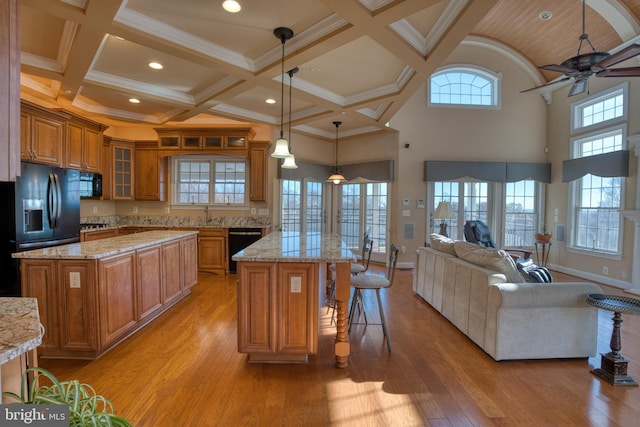 kitchen with brown cabinetry, glass insert cabinets, open floor plan, a center island, and pendant lighting