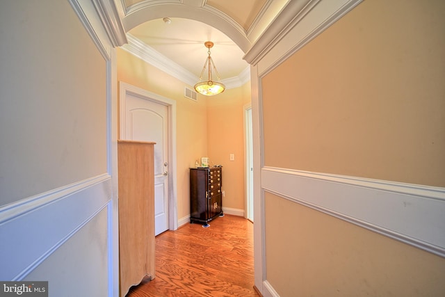 hallway featuring arched walkways, wood finished floors, visible vents, baseboards, and crown molding