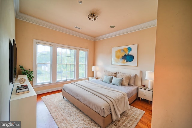 bedroom with light wood-style flooring, visible vents, and ornamental molding