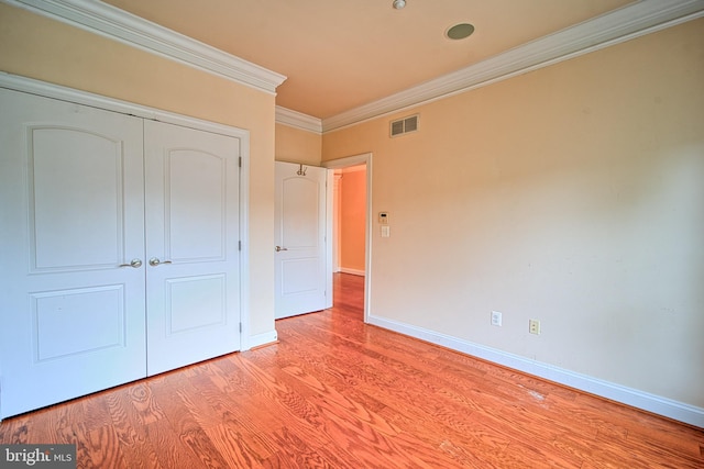 unfurnished bedroom featuring baseboards, visible vents, crown molding, light wood-style floors, and a closet