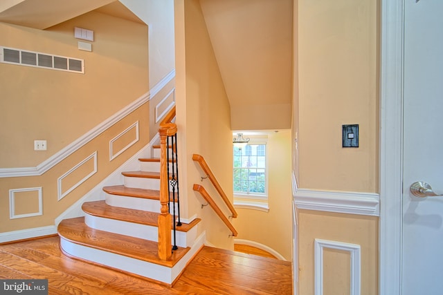 stairway featuring visible vents, a decorative wall, and wood finished floors