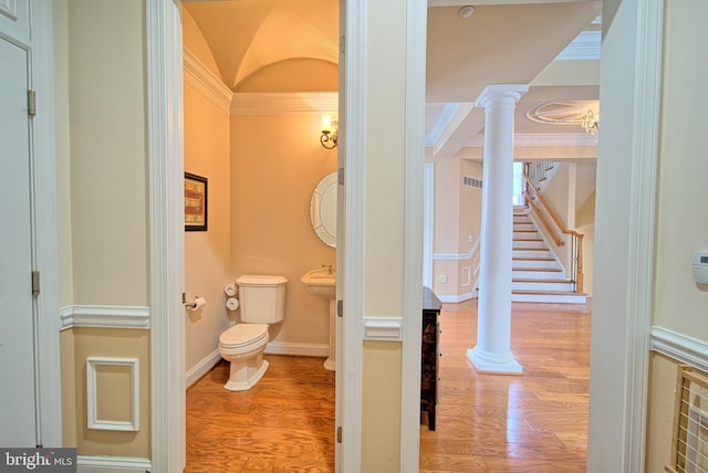 half bathroom with toilet, ornate columns, ornamental molding, and wood finished floors