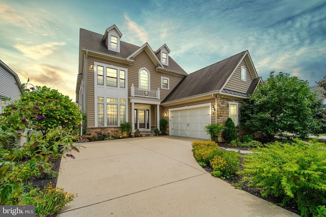 view of front facade featuring stone siding, driveway, an attached garage, and a balcony