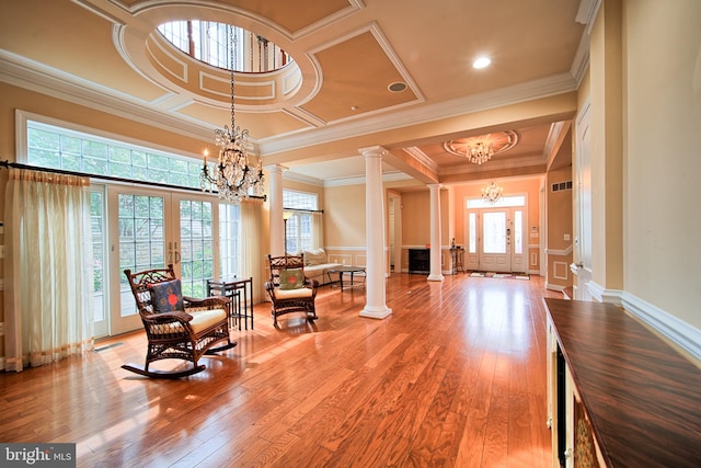 living area featuring decorative columns, light wood-style flooring, a notable chandelier, and french doors