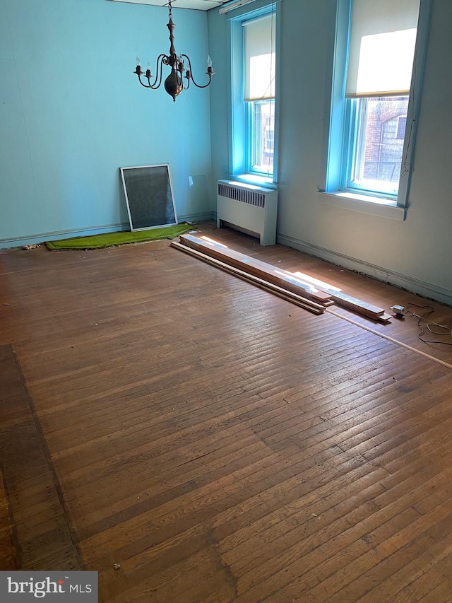 spare room with hardwood / wood-style floors, radiator, and an inviting chandelier