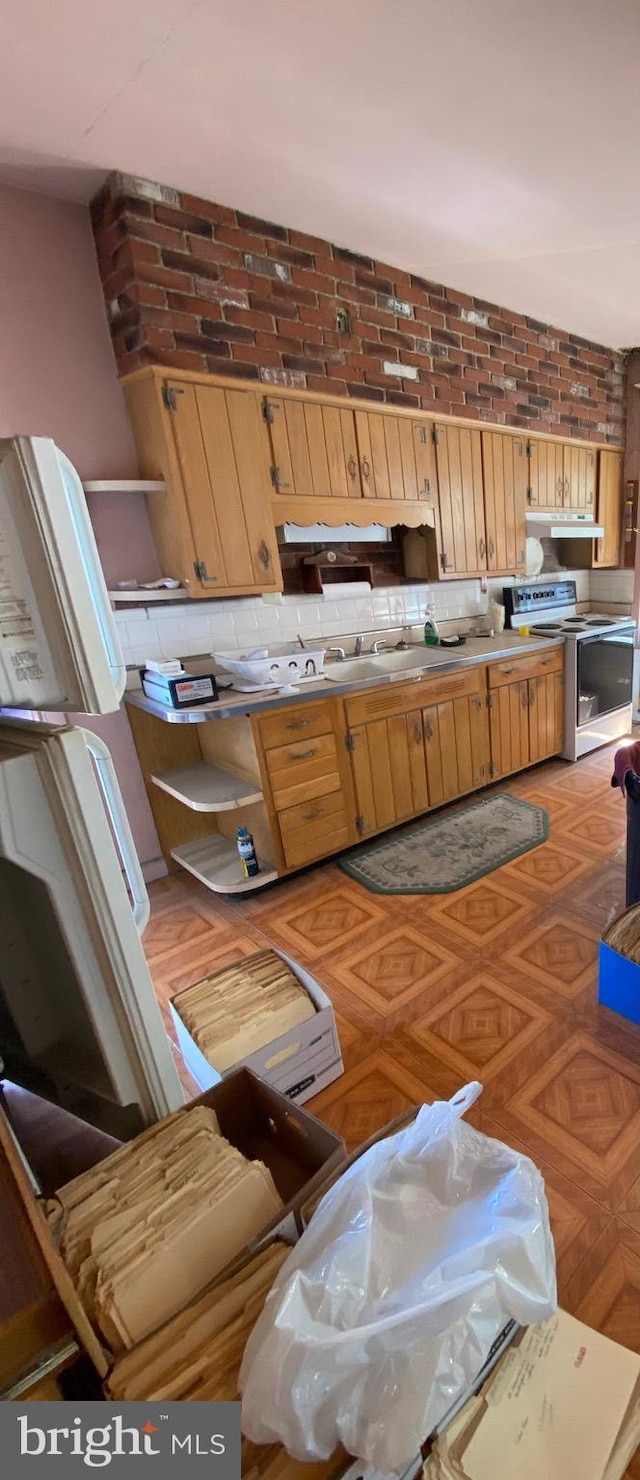 kitchen featuring parquet flooring, backsplash, sink, white range with electric stovetop, and brick wall