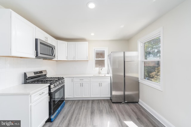 kitchen featuring stainless steel appliances, backsplash, light hardwood / wood-style flooring, and white cabinetry