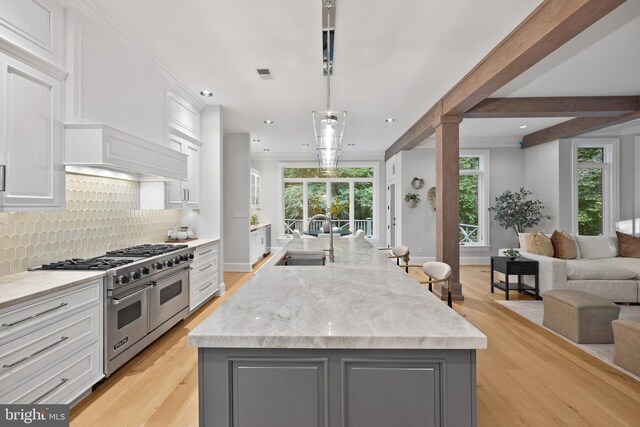 kitchen featuring sink, a spacious island, range with two ovens, light stone counters, and white cabinetry