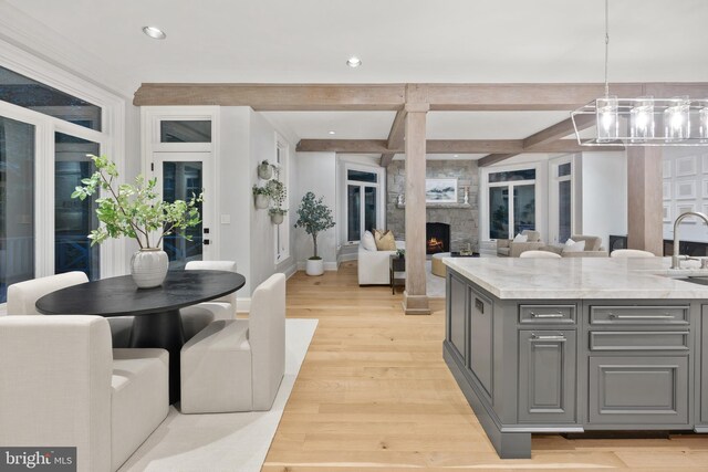 kitchen featuring light hardwood / wood-style flooring, a stone fireplace, an island with sink, light stone counters, and decorative light fixtures