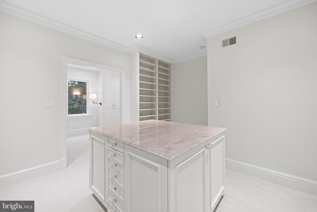 kitchen with ornamental molding, light stone countertops, white cabinets, a center island, and light carpet