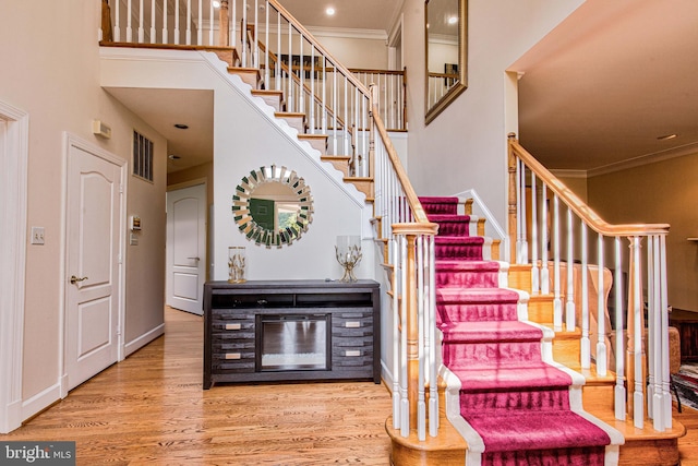 staircase featuring wood-type flooring, a towering ceiling, and crown molding