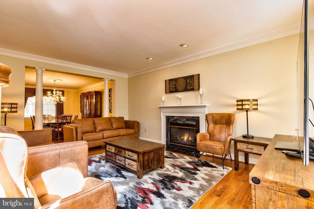 living room featuring a notable chandelier, crown molding, decorative columns, and hardwood / wood-style floors