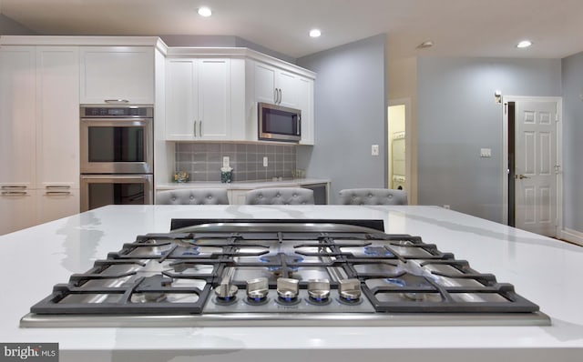 interior space with stainless steel appliances, light stone counters, white cabinets, and backsplash