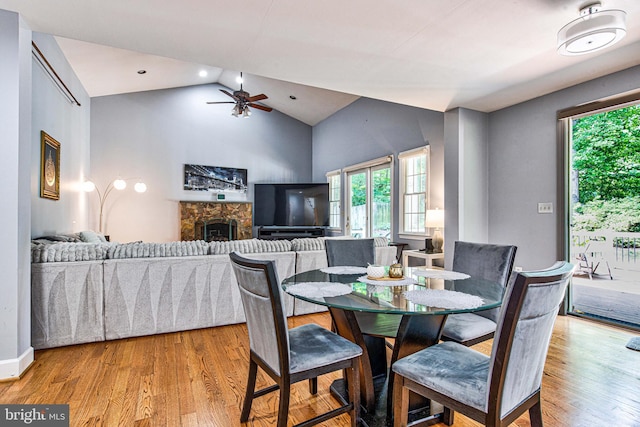 dining area featuring ceiling fan, a fireplace, vaulted ceiling, and light hardwood / wood-style flooring