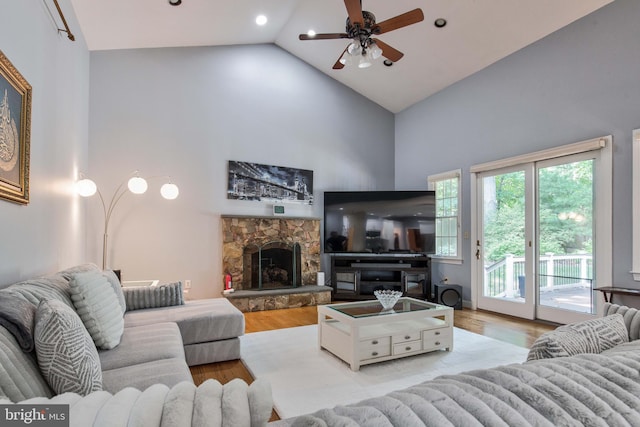 living room featuring a stone fireplace, light hardwood / wood-style flooring, high vaulted ceiling, and ceiling fan