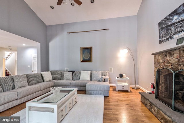 living room featuring a stone fireplace, high vaulted ceiling, ceiling fan, and light wood-type flooring