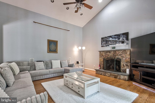 living room featuring hardwood / wood-style flooring, ceiling fan, a stone fireplace, and high vaulted ceiling