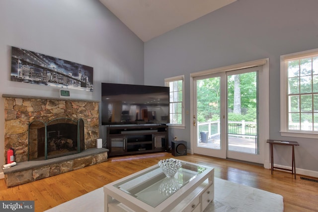 living room with hardwood / wood-style flooring, a stone fireplace, and high vaulted ceiling